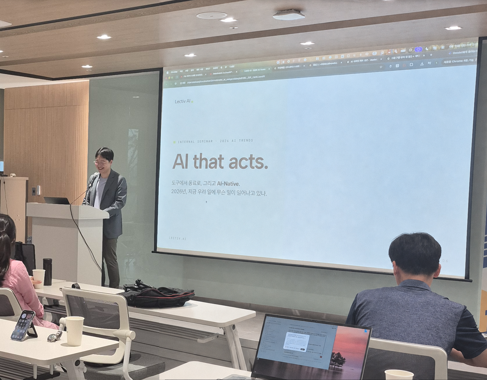 Mark Kim presenting on a stage with the words AI that acts behind him